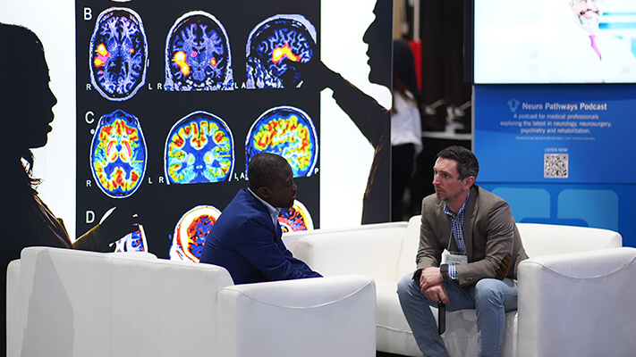 Two men having conversation in front of large exhibit of brain scans