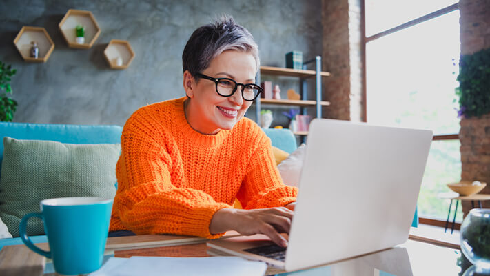 Woman on laptop in casual setting registering for AAN Annual Meeting