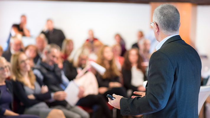 Man in a suit presenting to a room of meeting attendees